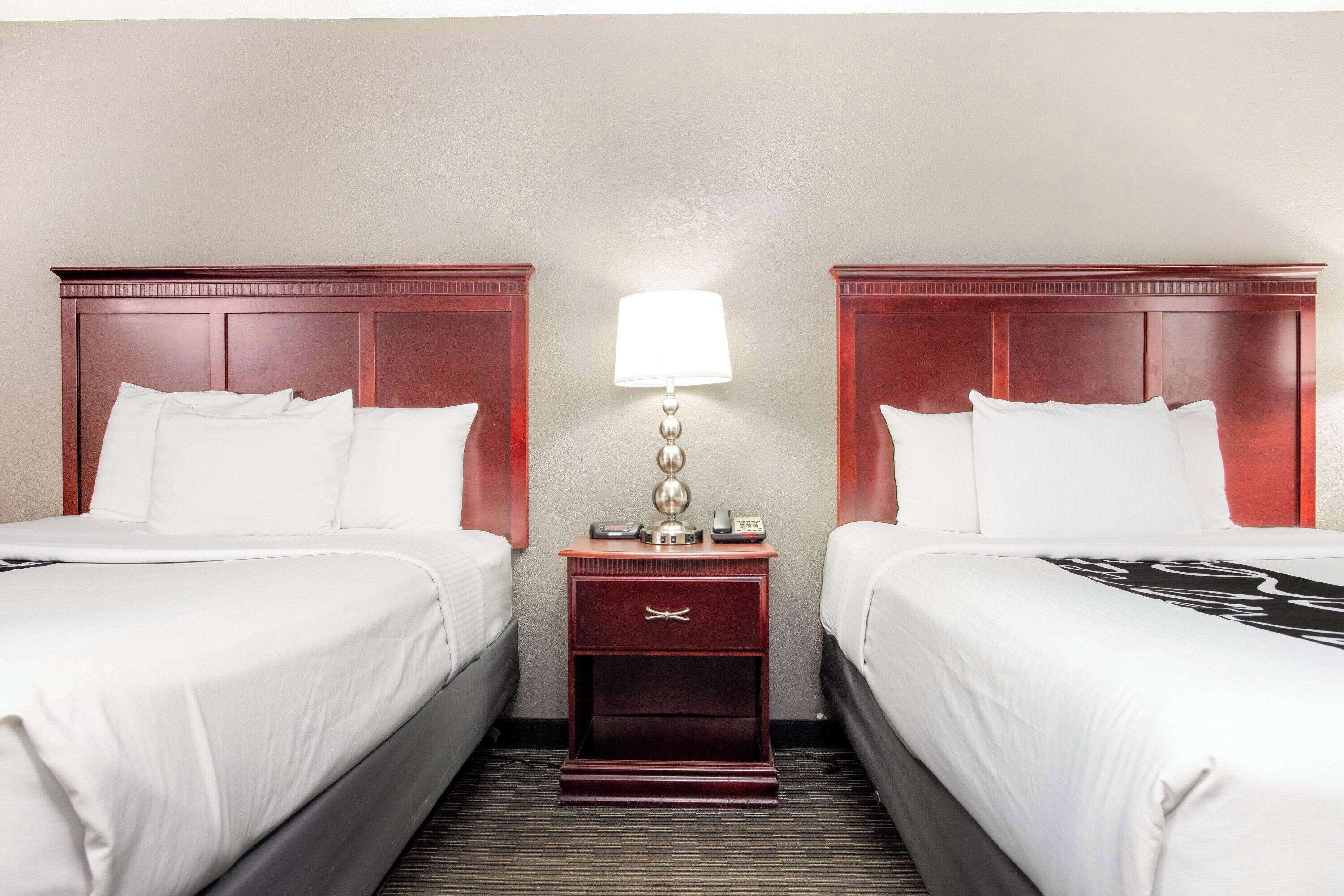 A hotel room with two beds, a nightstand with a lamp, and a telephone.