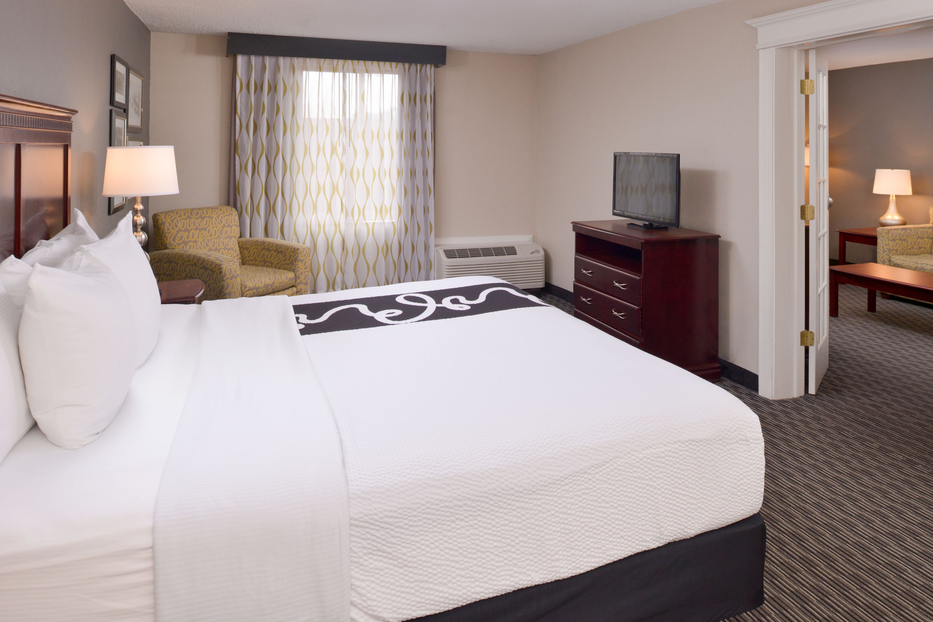A hotel room with a large bed, a chair, a television, and a desk.