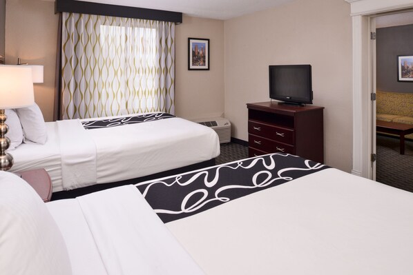 Habitación de hotel con dos camas, un televisor sobre un mueble de madera, un cuadro de un paisaje urbano en la pared y una alfombra estampada.