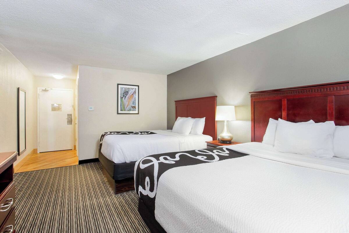 Ein Hotelzimmer mit zwei Betten, Holzboden, rotem Kopfteil und einem gerahmten Bild an der Wand.