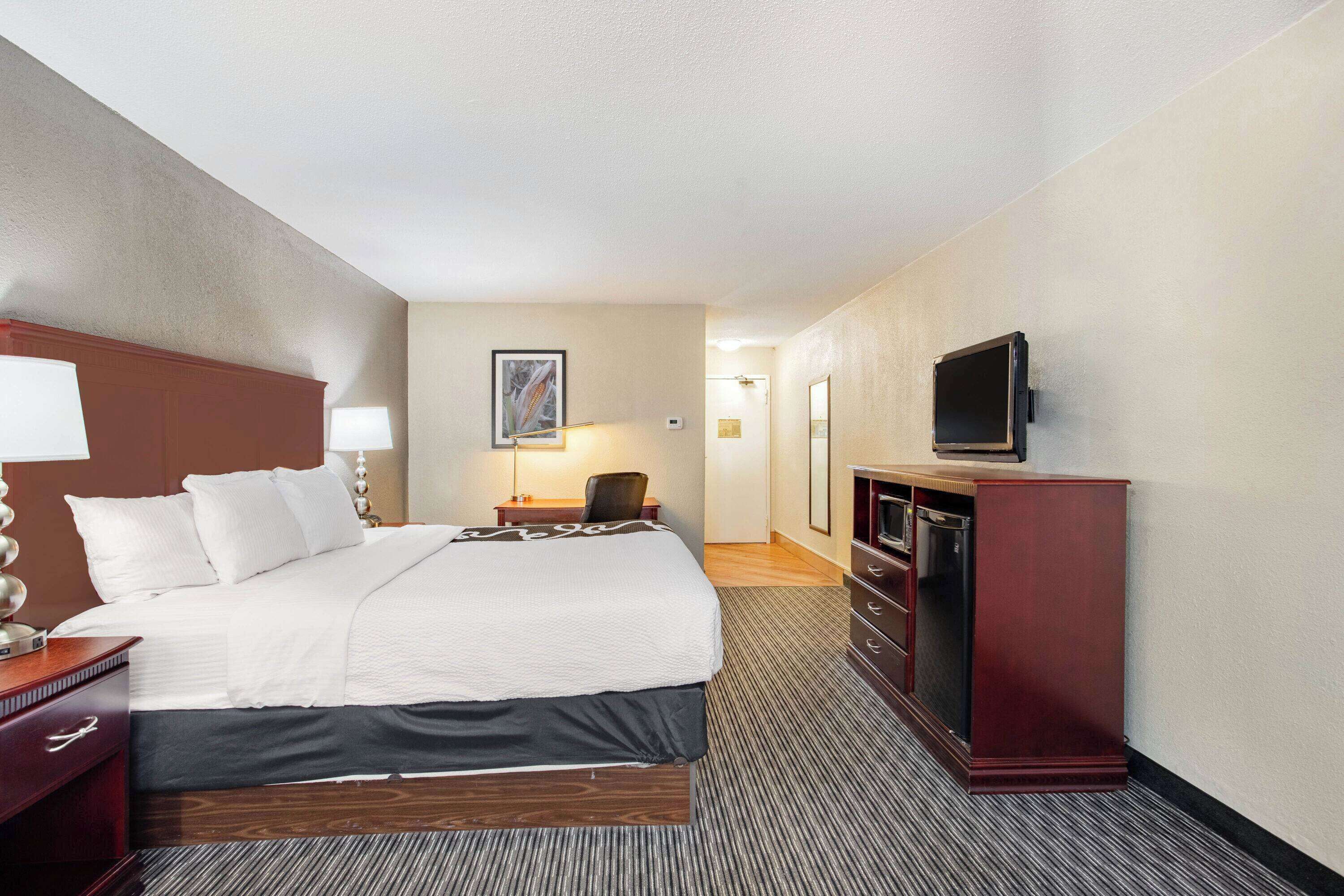 Een hotelkamer met een groot bed, een bureau met lamp, een televisie op een standaard en een dressoir.