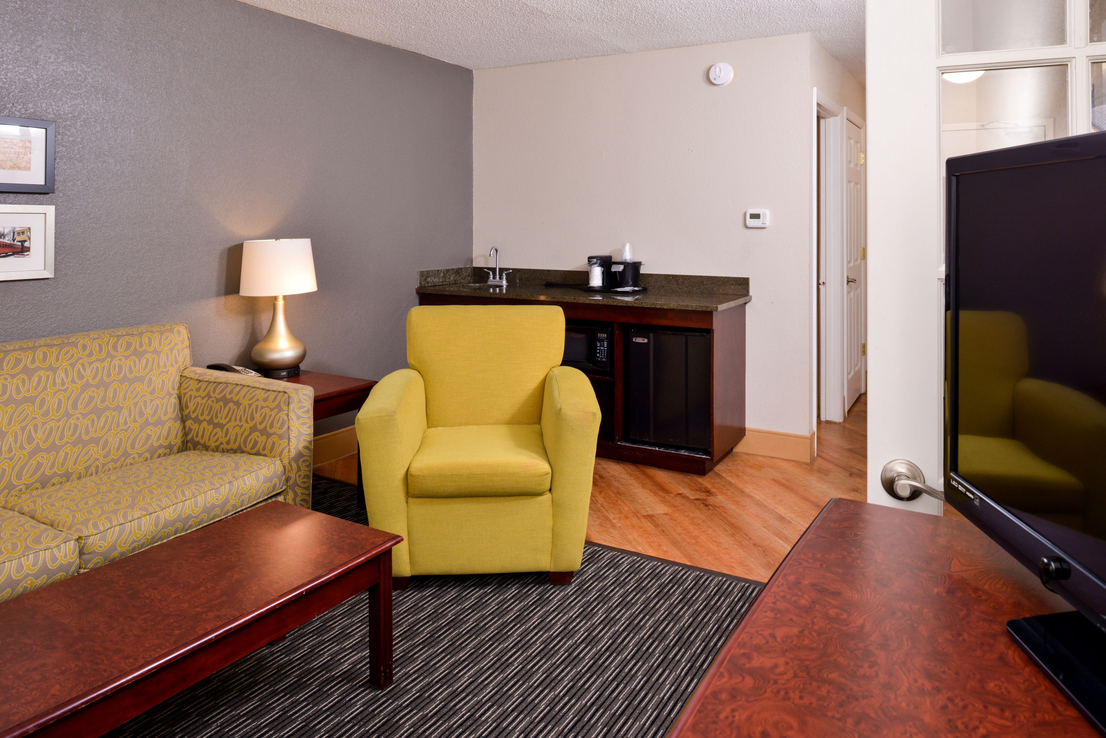 A compact living space with a sofa, a yellow armchair, a coffee maker, and a television.