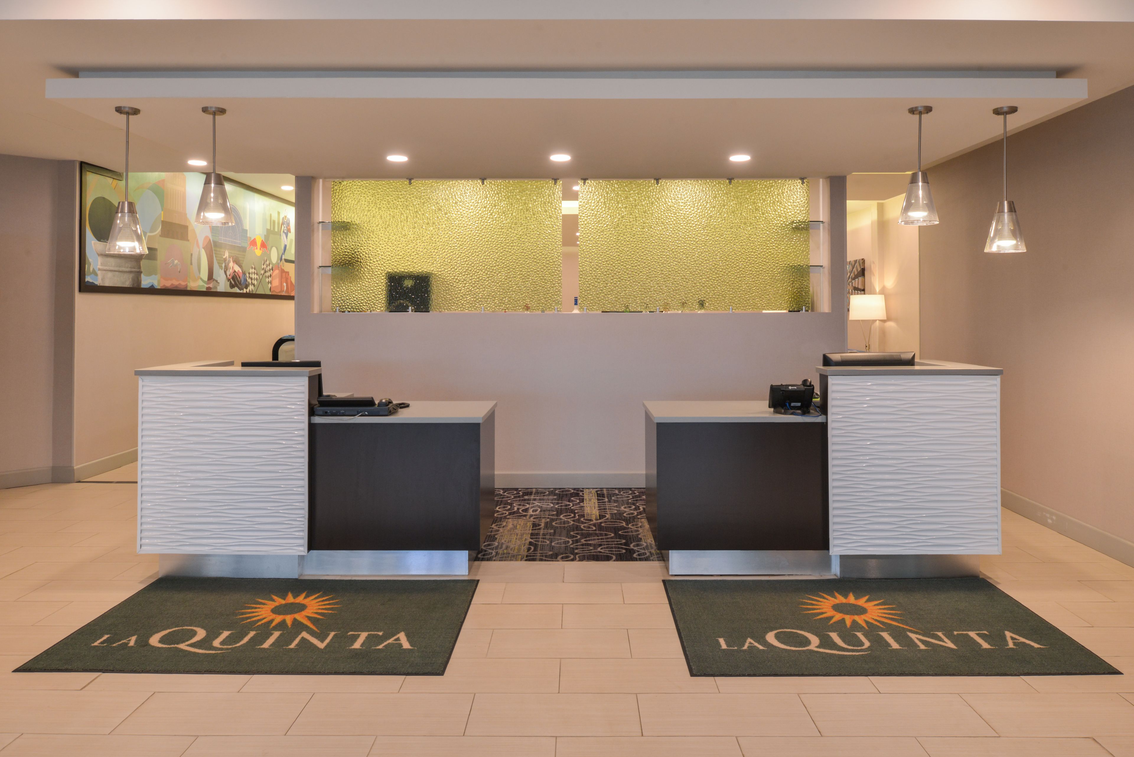 A reception area with two counters, a textured glass wall, and a patterned carpet with "La Quinta" branding.