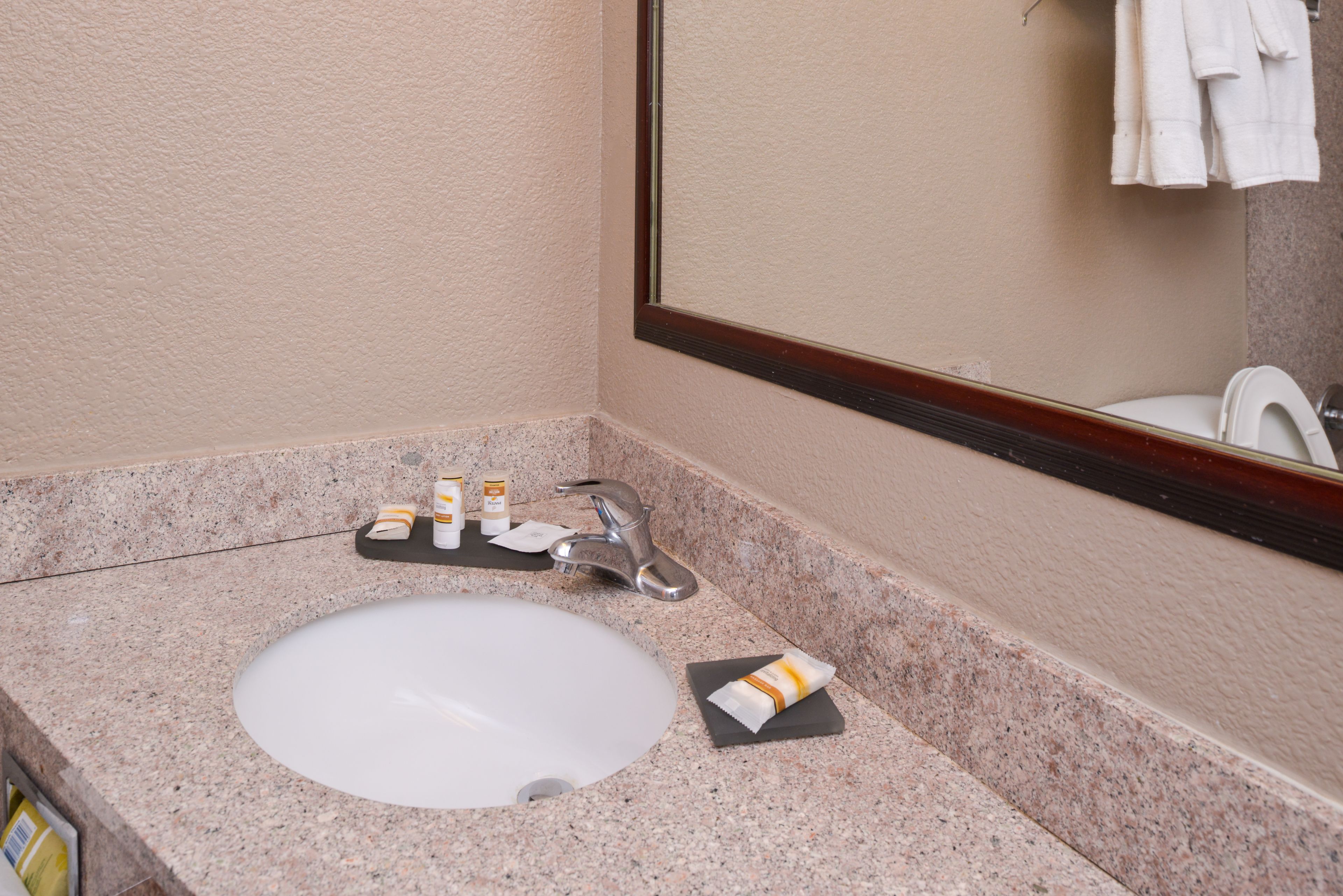 Une salle de bain avec un comptoir en granit, un lavabo blanc, un miroir et un porte-serviettes.