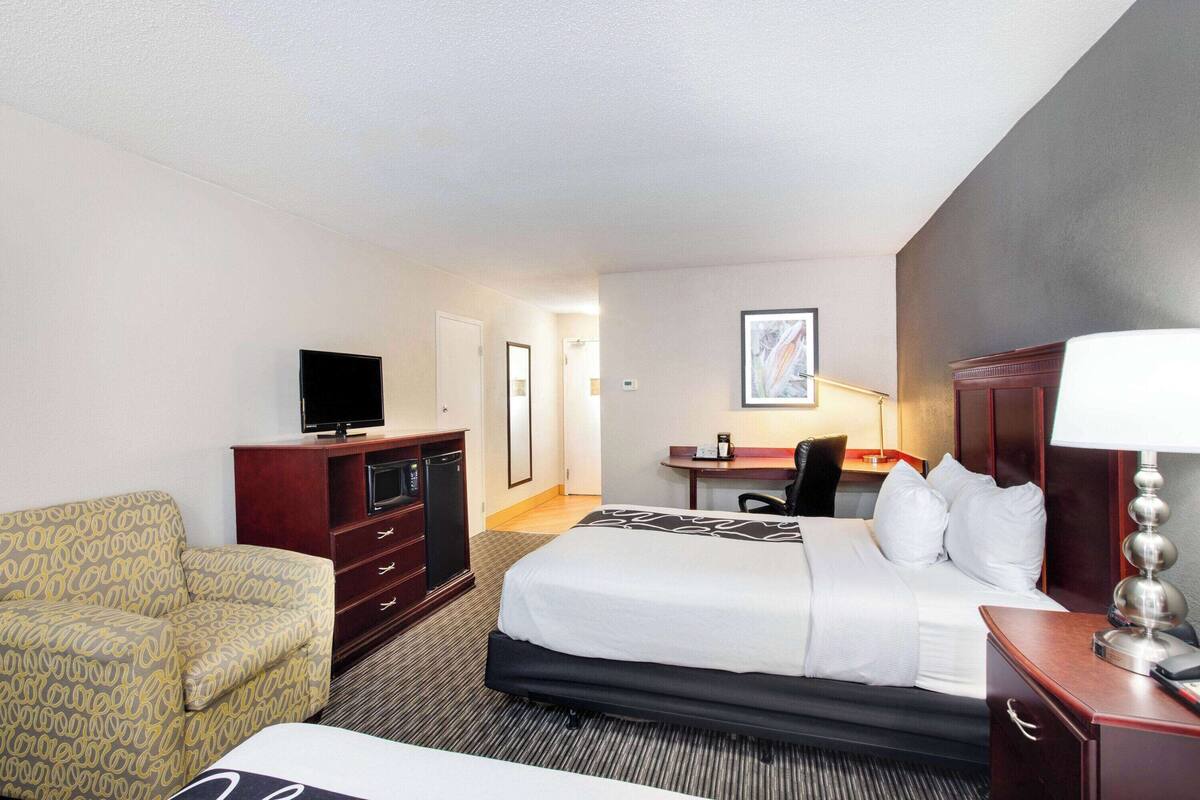 Ein Hotelzimmer mit Bett, Schreibtisch, Fernseher, Sessel und Lampe.