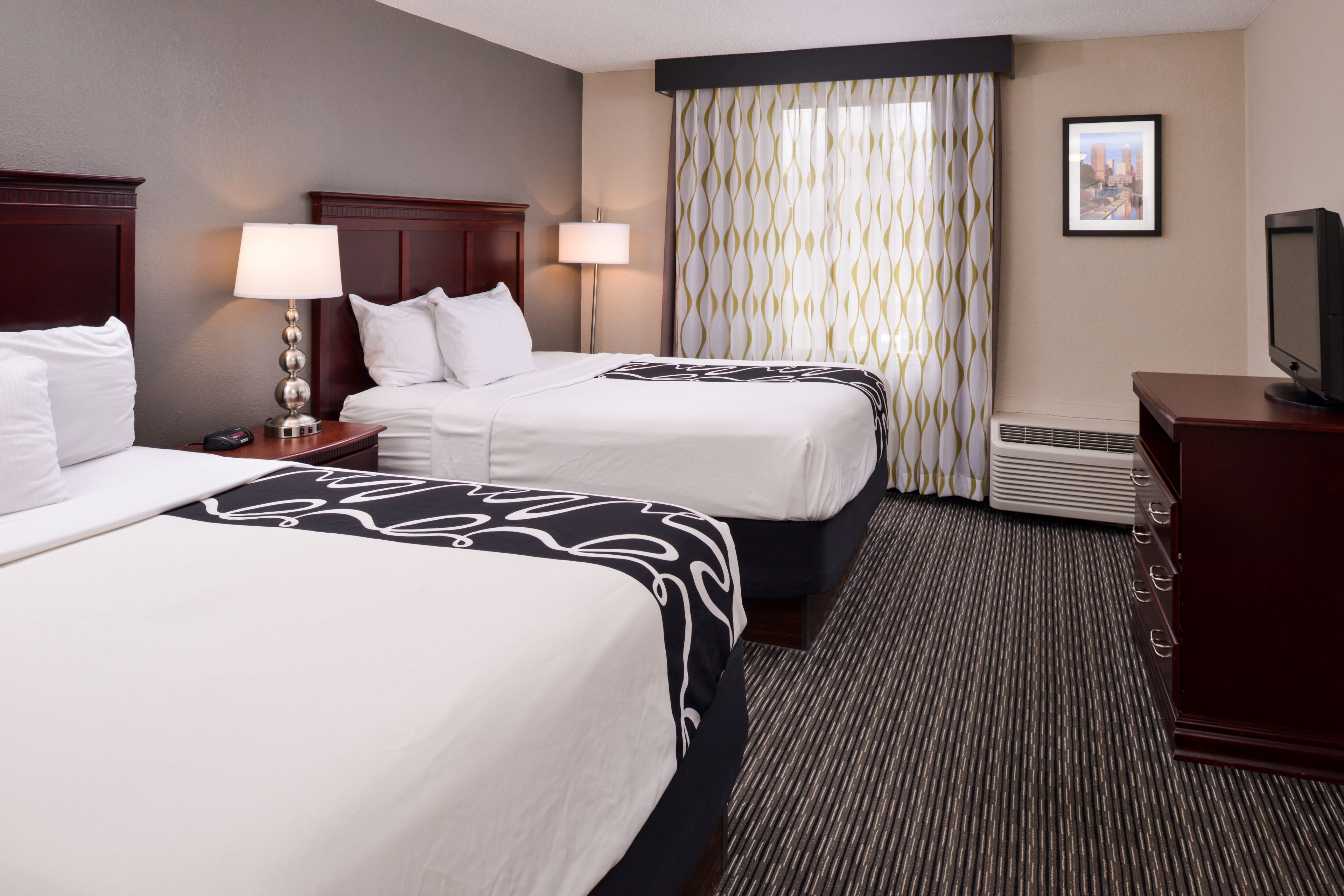 A hotel room with two beds, a desk, a television, and a picture on the wall.