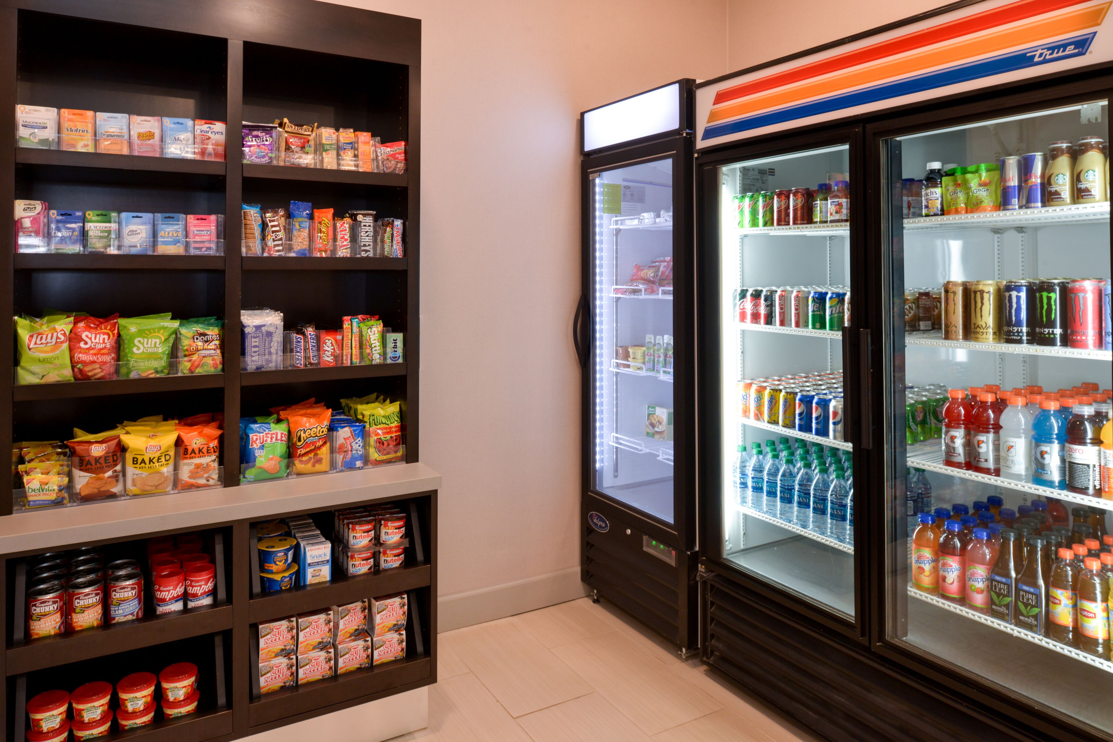 A self-service beverage and snack area with refrigerated drinks and various packaged snacks.