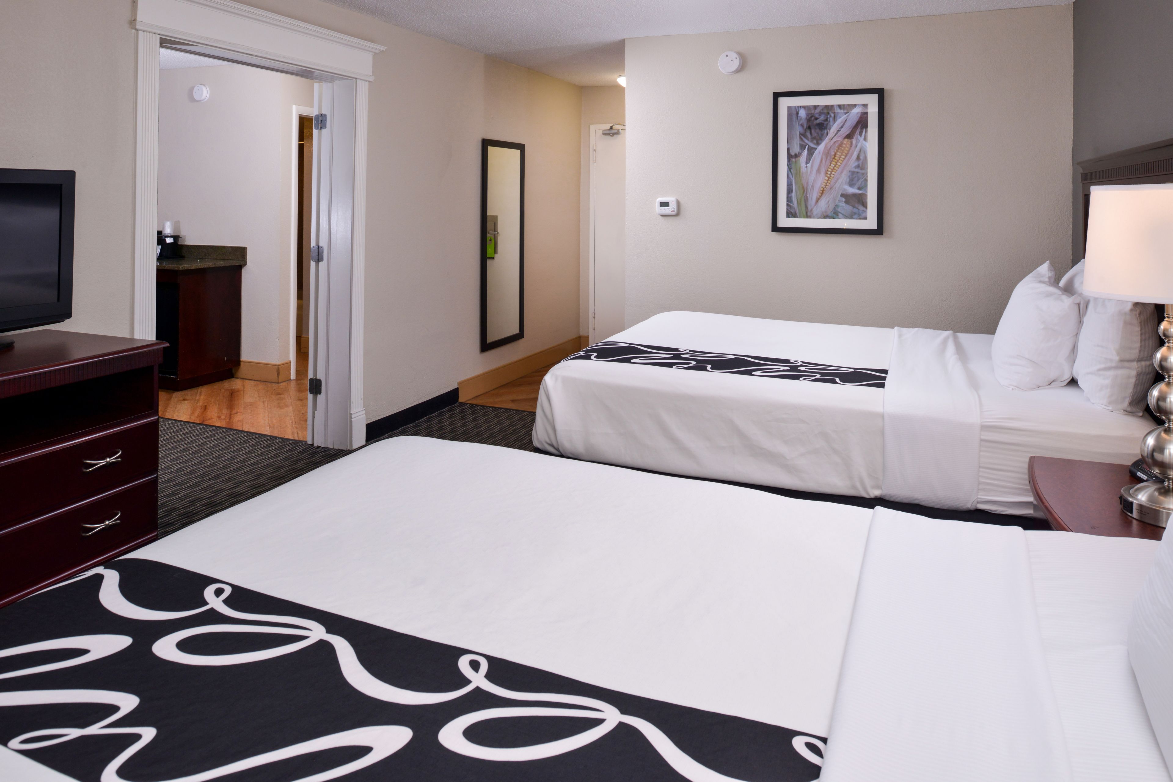 A hotel room with two beds, a TV, a desk, and a bathroom visible through an open door.