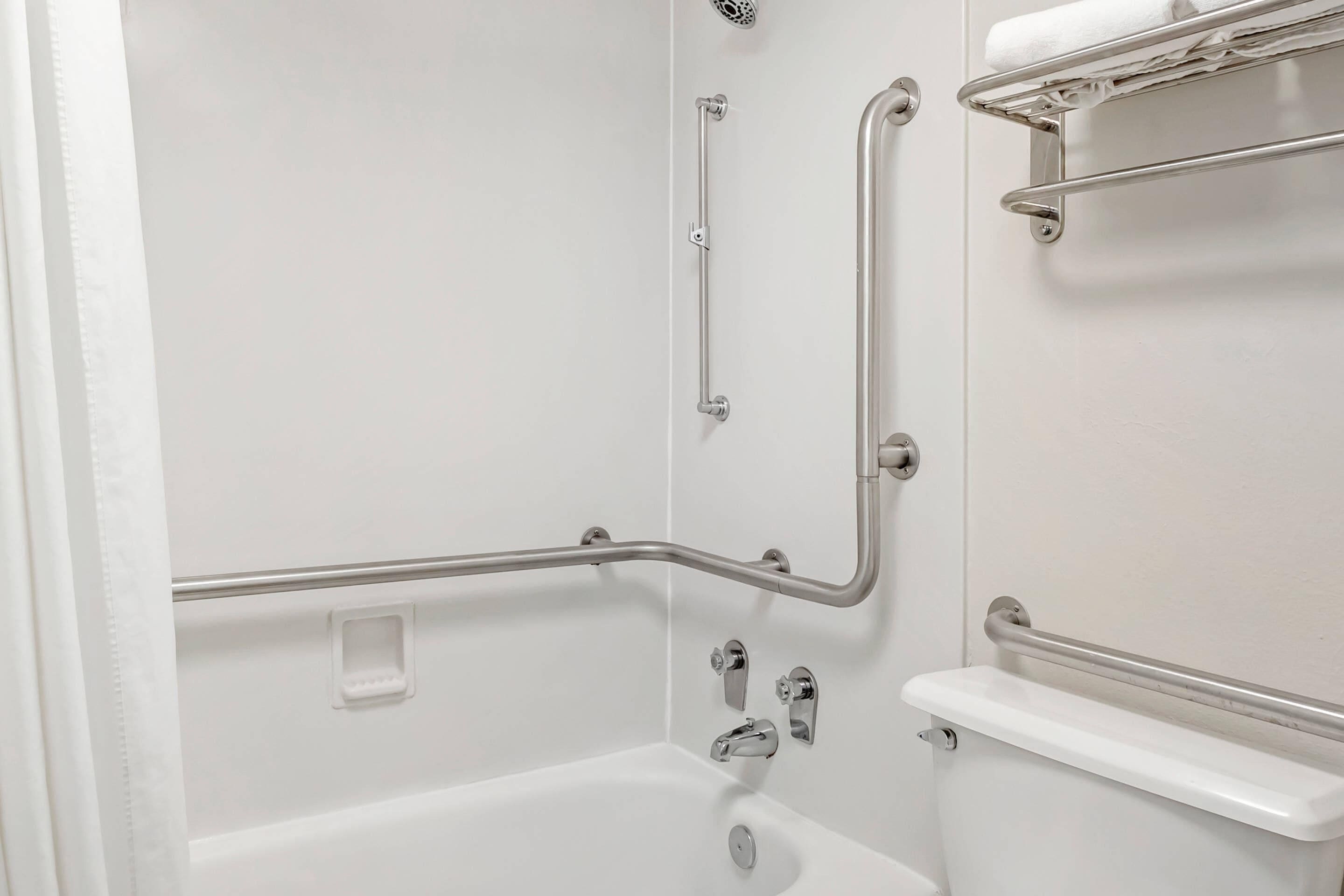 A bathroom with a white bathtub, a shower, and a toilet. It includes grab bars and a towel rack.