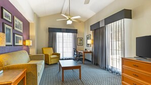 A hotel room with a sofa, armchair, desk, television, and a ceiling fan. - Quality Inn & Suites North Charleston - Ashley Phosphate (North Charleston)