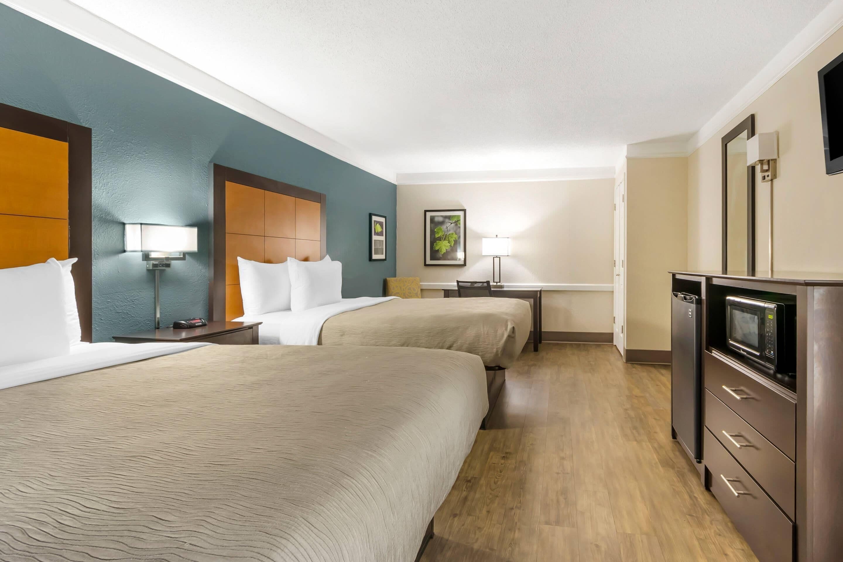 A hotel room with two beds, a desk, a microwave, and a TV.