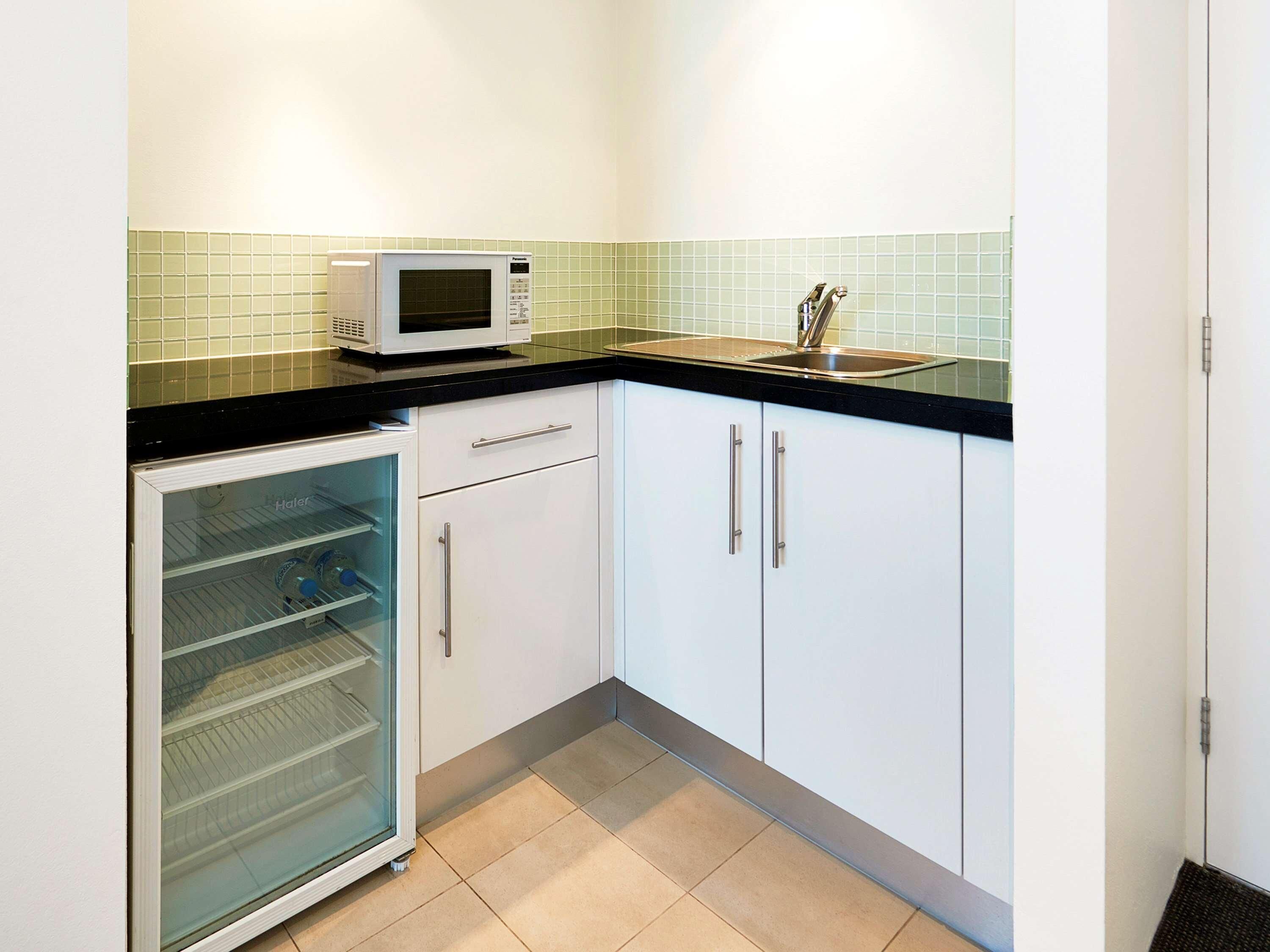 A compact kitchen with white cabinets, a black countertop, a microwave, and a glass-fronted refrigerator.