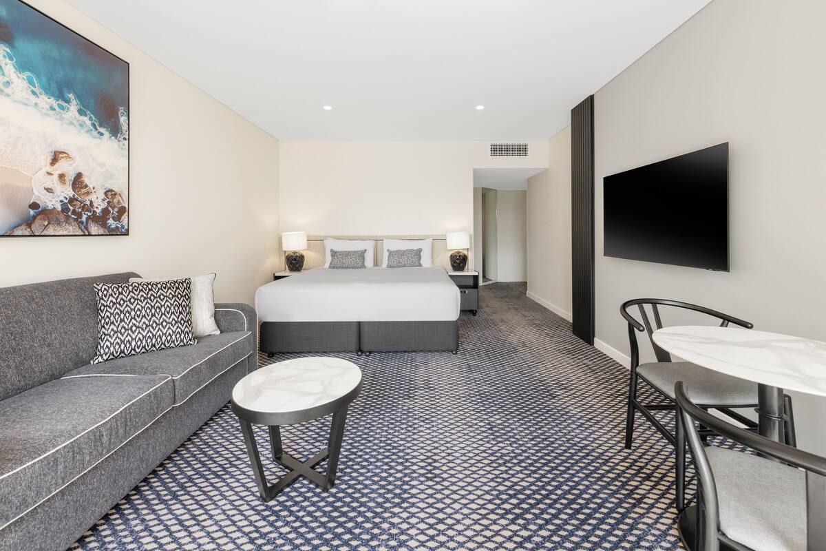 A hotel room with a bed, a sofa, a small table, and a TV.
