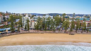 Paisagem costeira com uma praia arenosa, edifícios e árvores.