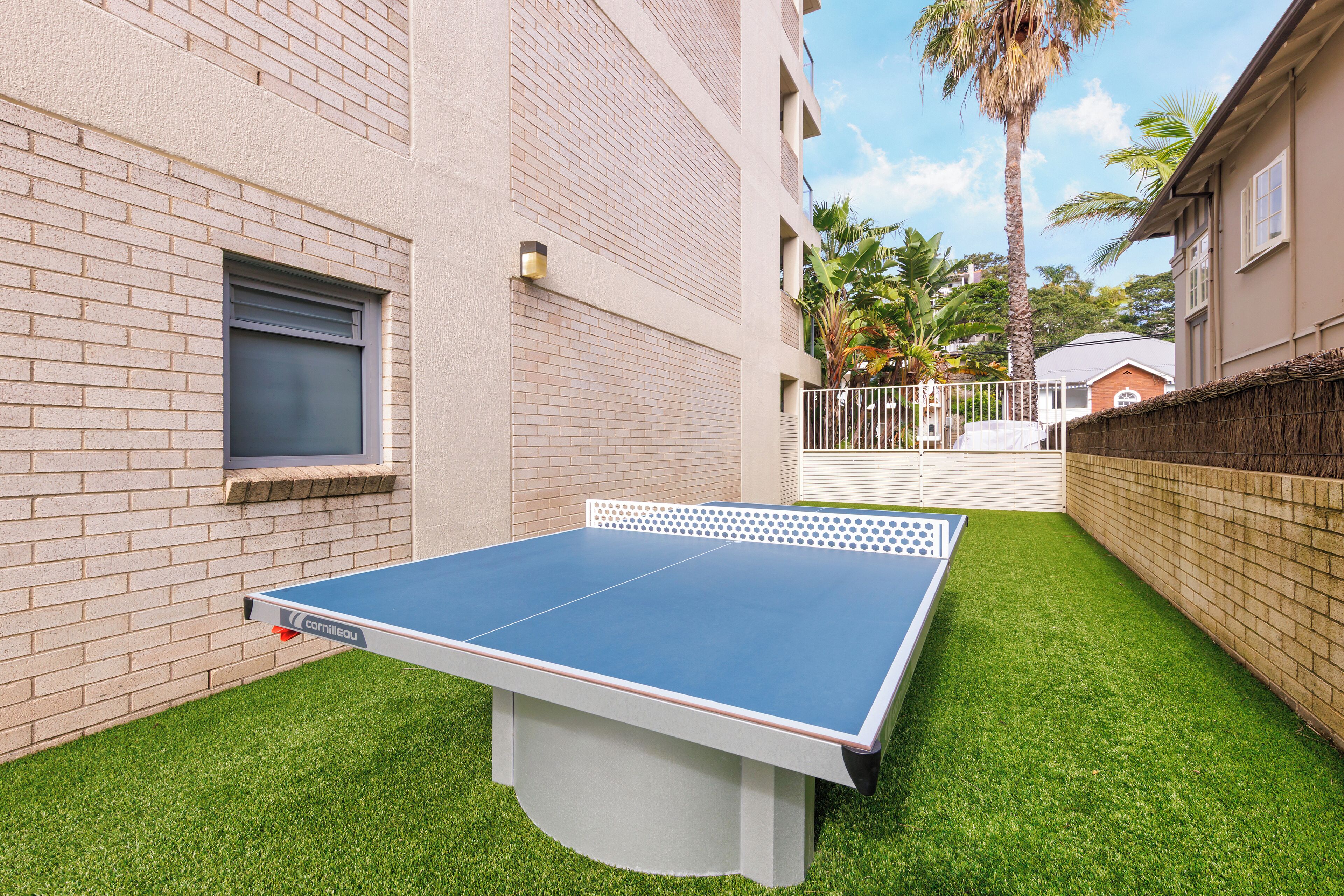 Une table de ping-pong dans une cour, avec un mur de briques et un palmier en arrière-plan.