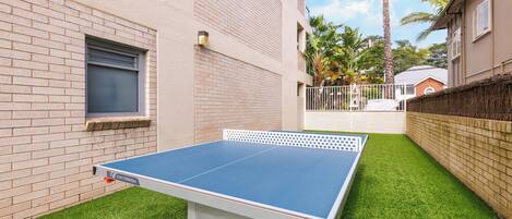 Une table de ping-pong dans une cour, avec un mur de briques et un palmier en arrière-plan.