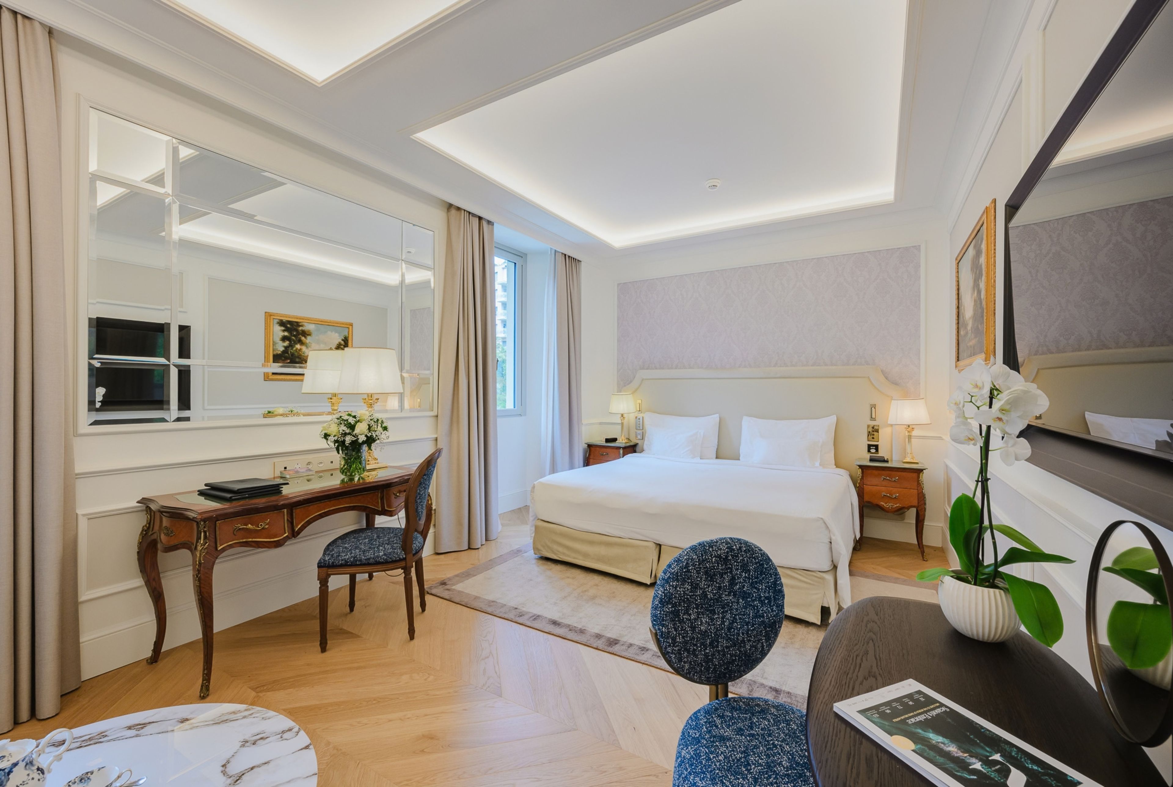 A hotel room with a bed, a desk, a chair, a mirror, and a window.