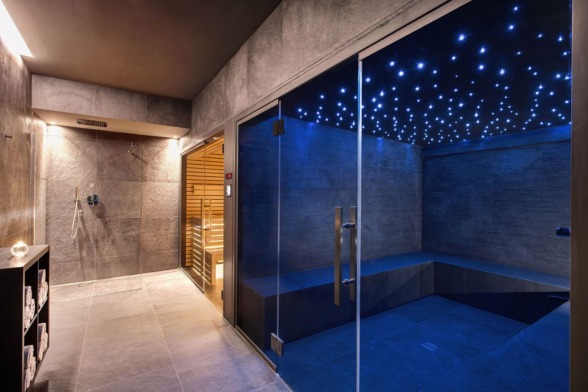 A modern bathroom with a glass-enclosed shower, a wooden bench, and a towel rack.