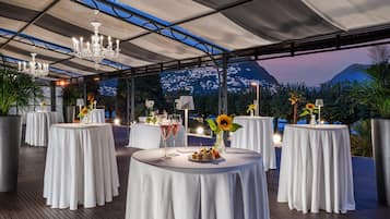 Ein Dachterrasse-Essbereich mit runden Tischen, gedeckt mit weißen Tischdecken, jeweils mit Kerze und Blumenarrangements.