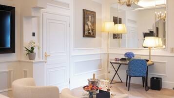 Una habitación bien iluminada con una puerta blanca, un retrato enmarcado, una mesa con fruteros, una botella de champán y una silla azul.