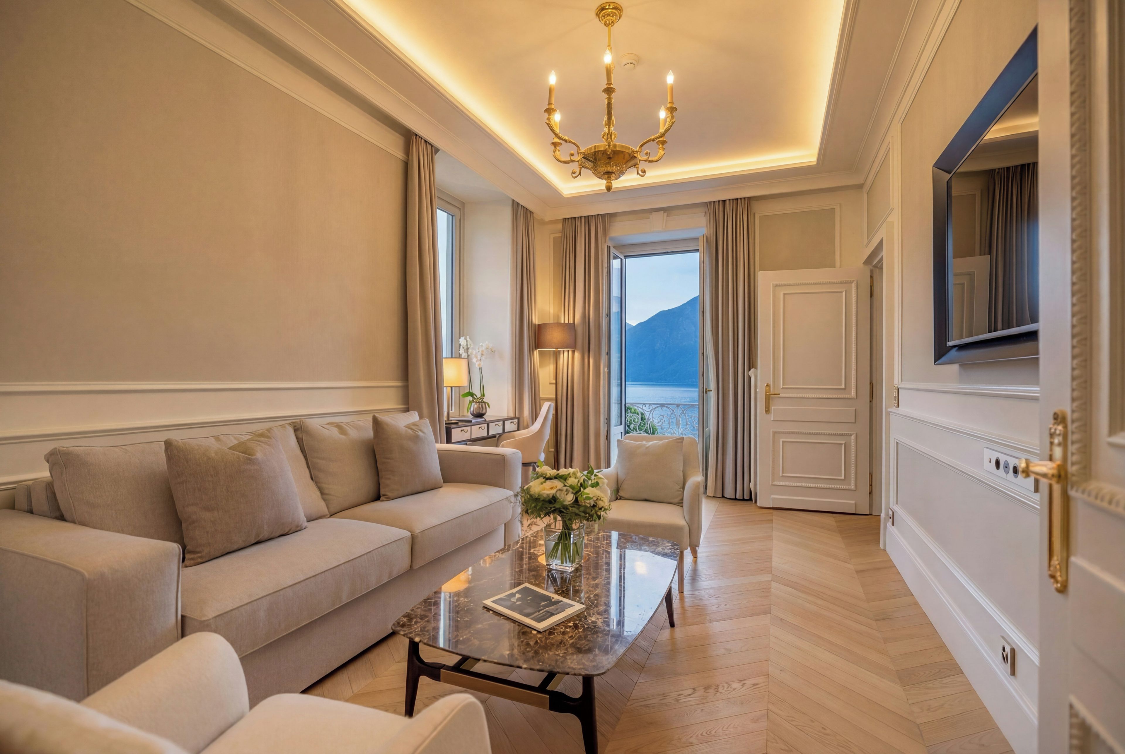 A hotel room with a sofa, a coffee table with a book, a lamp, and a view of the sea.