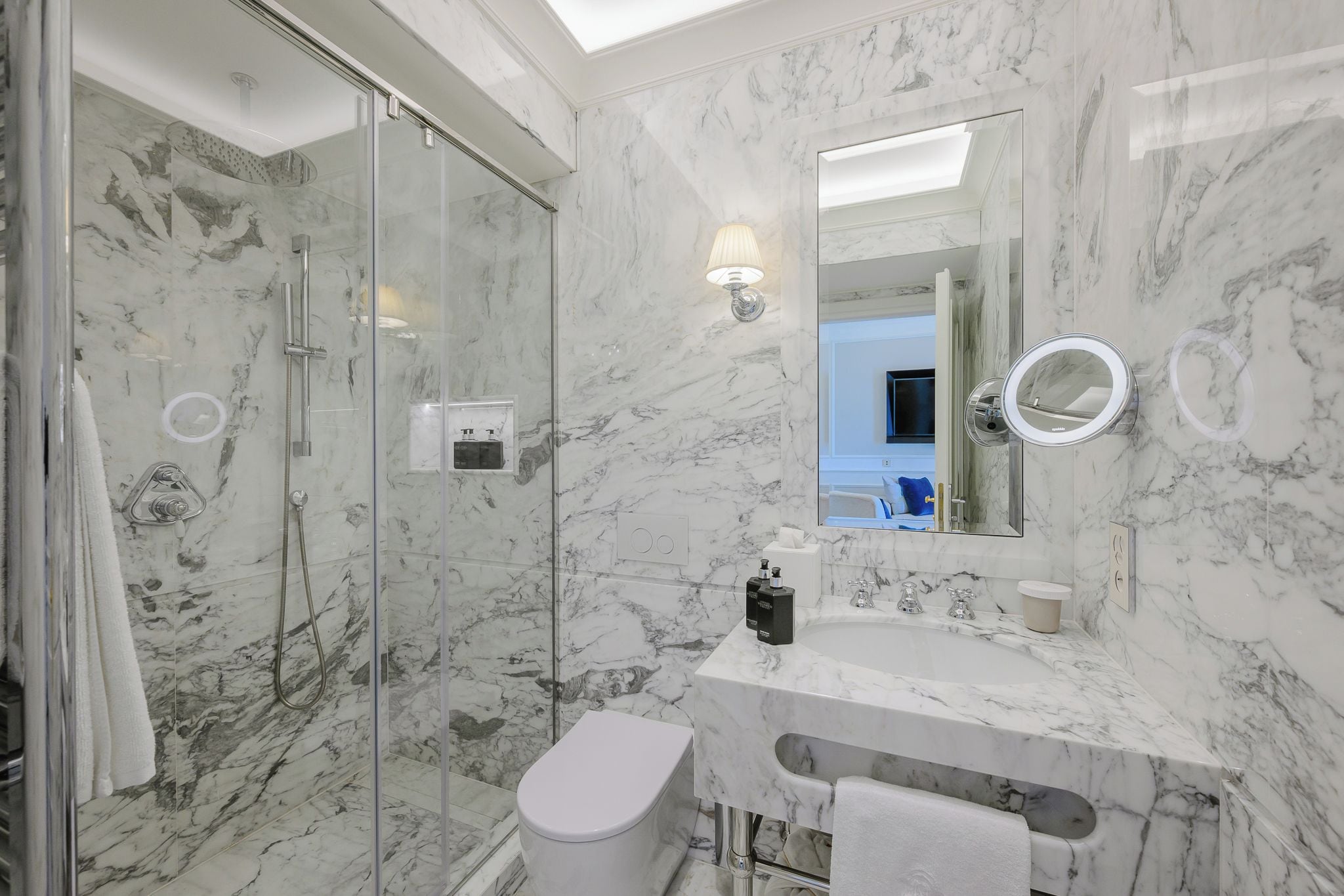 Une salle de bain moderne avec une douche à parois de verre, un lavabo en marbre et un grand miroir.