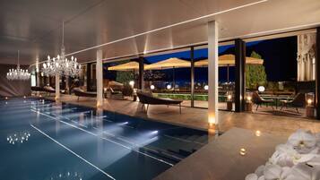 Un área de piscina interior moderna con vistas despejadas al exterior, sillones de descanso y un candelabro.
