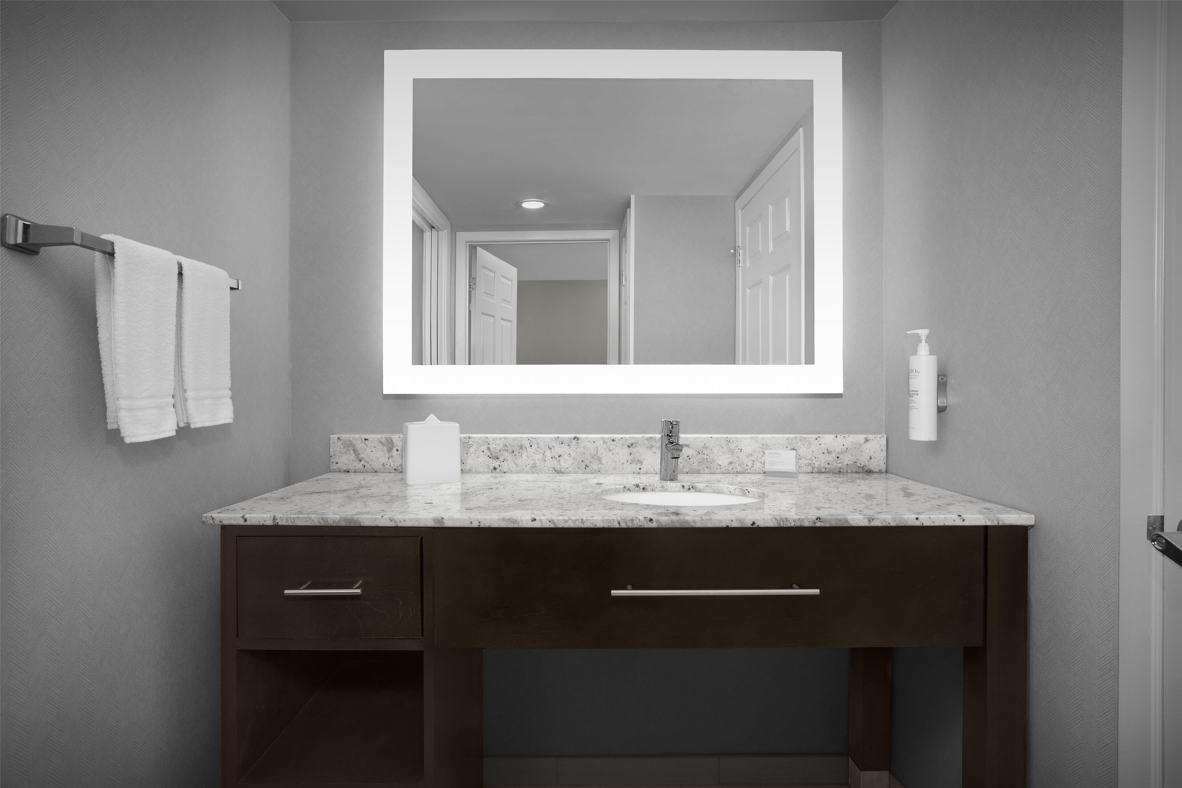 Un baño con lavamanos de mármol, muebles oscuros, un espejo grande y un perchero para toallas.