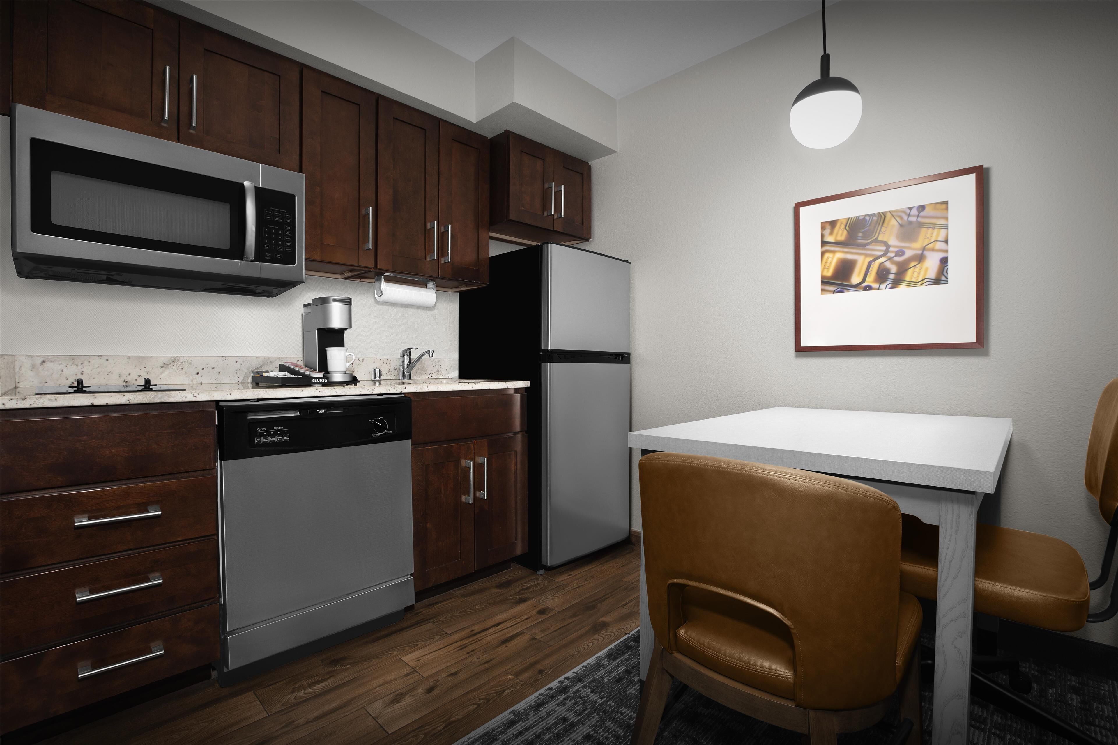 Una cocina moderna con armarios de madera, electrodomésticos de acero inoxidable, encimera blanca y un comedor con mesa y sillas.