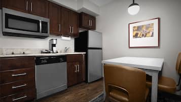 Una cocina moderna con armarios de madera, electrodomésticos de acero inoxidable, encimera blanca y un comedor con mesa y sillas.
