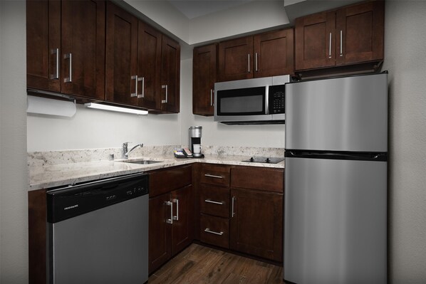 A modern kitchen with dark wooden cabinets, stainless steel appliances, and a granite countertop.