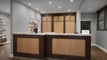 Un espace d’accueil d’hôtel avec un comptoir de réception en bois, un minibar et un panneau indiquant l’adhésion au programme Hilton Honors.
