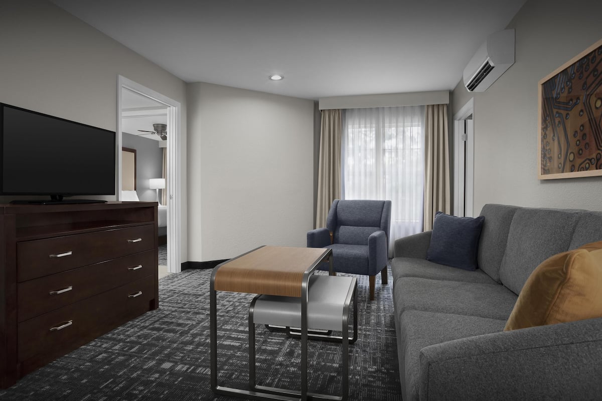 A hotel room with a flat-screen TV, a sofa, a chair, a small table, and a wardrobe.