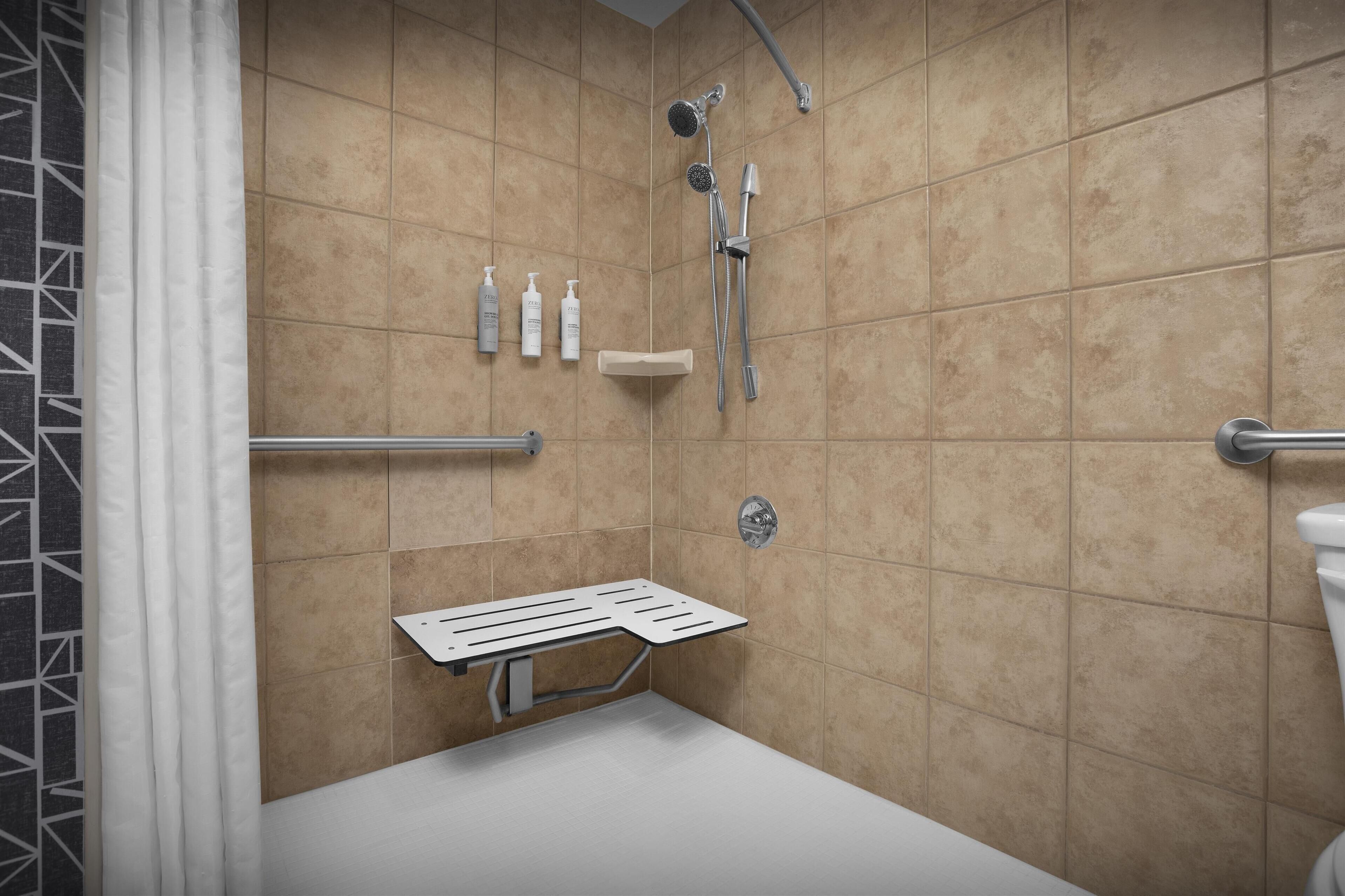 Un bagno moderno rivestito di piastrelle color beige, con una doccia dotata di soffione manuale.