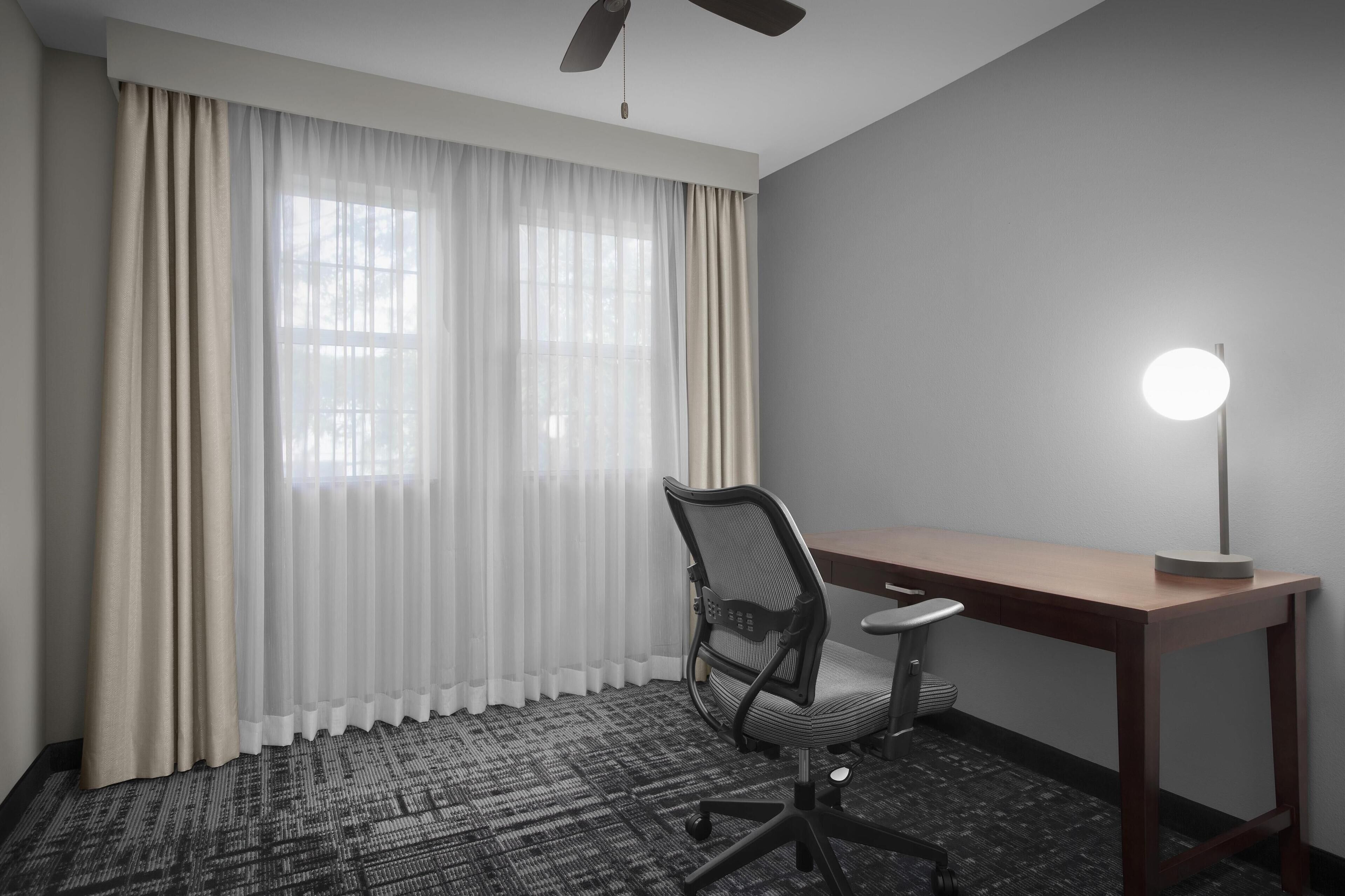 Ein Hotelzimmer mit Schreibtisch, Stuhl und Deckenventilator.