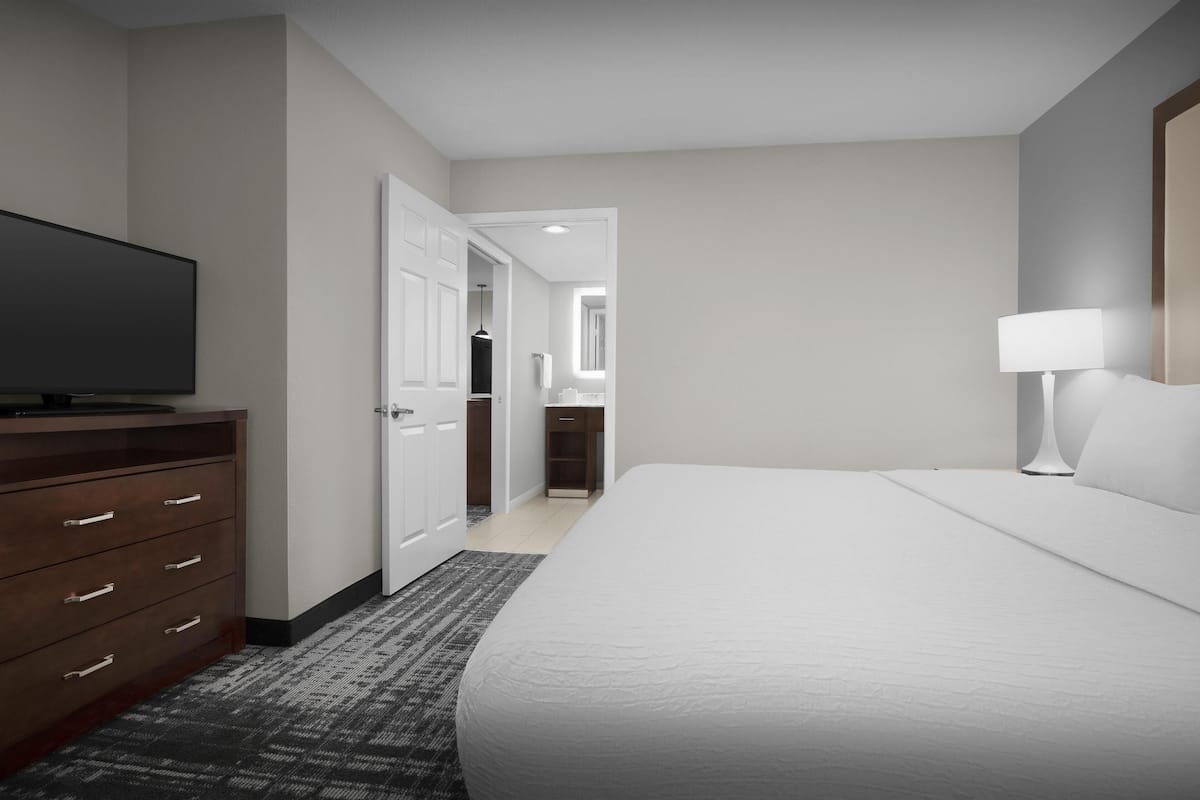 A hotel room with a large bed, a TV on a wooden dresser, a lamp, and a door leading to a bathroom.