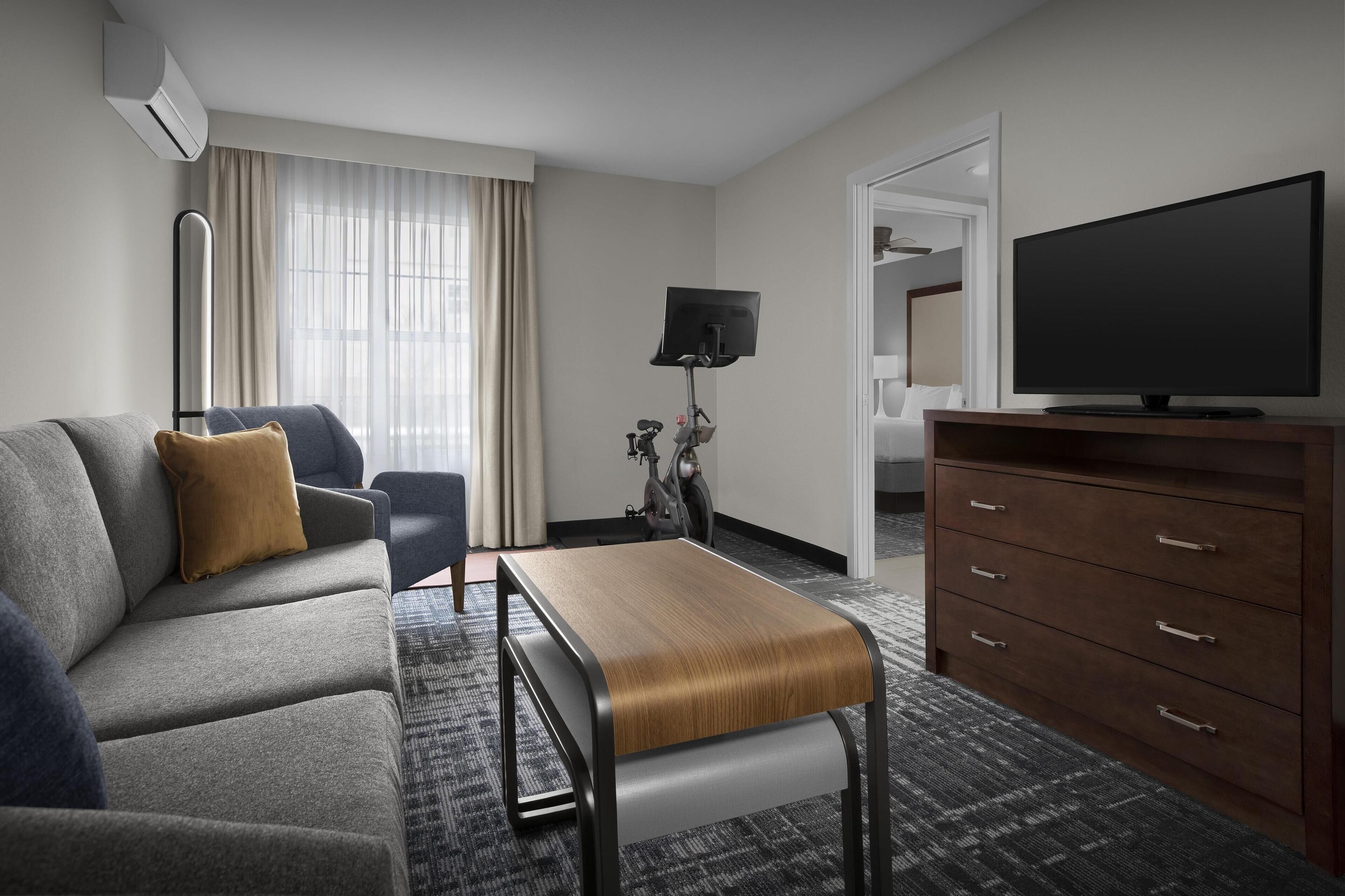 Ein modernes Hotelzimmer mit einer Sitzecke, einer Holzbank, einem Fernseher, einem Schreibtisch und einer Lampe.