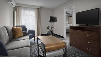Ein modernes Hotelzimmer mit einer Sitzecke, einer Holzbank, einem Fernseher, einem Schreibtisch und einer Lampe.