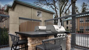 Un espace barbecue extérieur agrémenté de piliers en pierre, de deux fauteuils en osier et d’un gril.