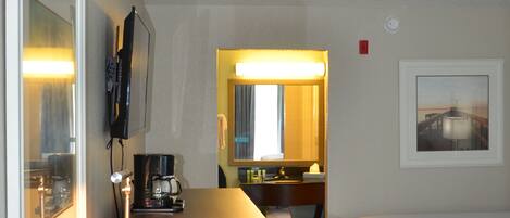 Una habitación de hotel con un escritorio de madera, una cama, un televisor montado en la pared y un cuadro enmarcado.