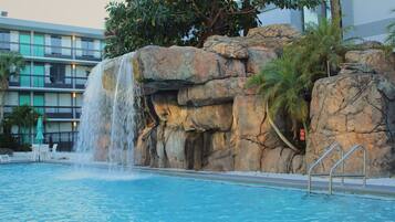 A pool with a waterfall feature, surrounded by large rocks and palm trees.