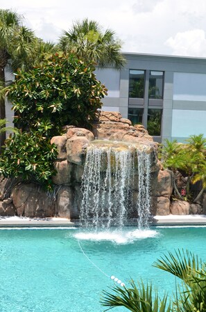 A clear blue pool with a waterfall feature surrounded by rocks and greenery. - Opal Hotel & Suites (Altamonte Springs)