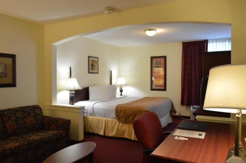 A hotel room with a bed, two bedside tables, a desk, a chair, a sofa, and a lamp.