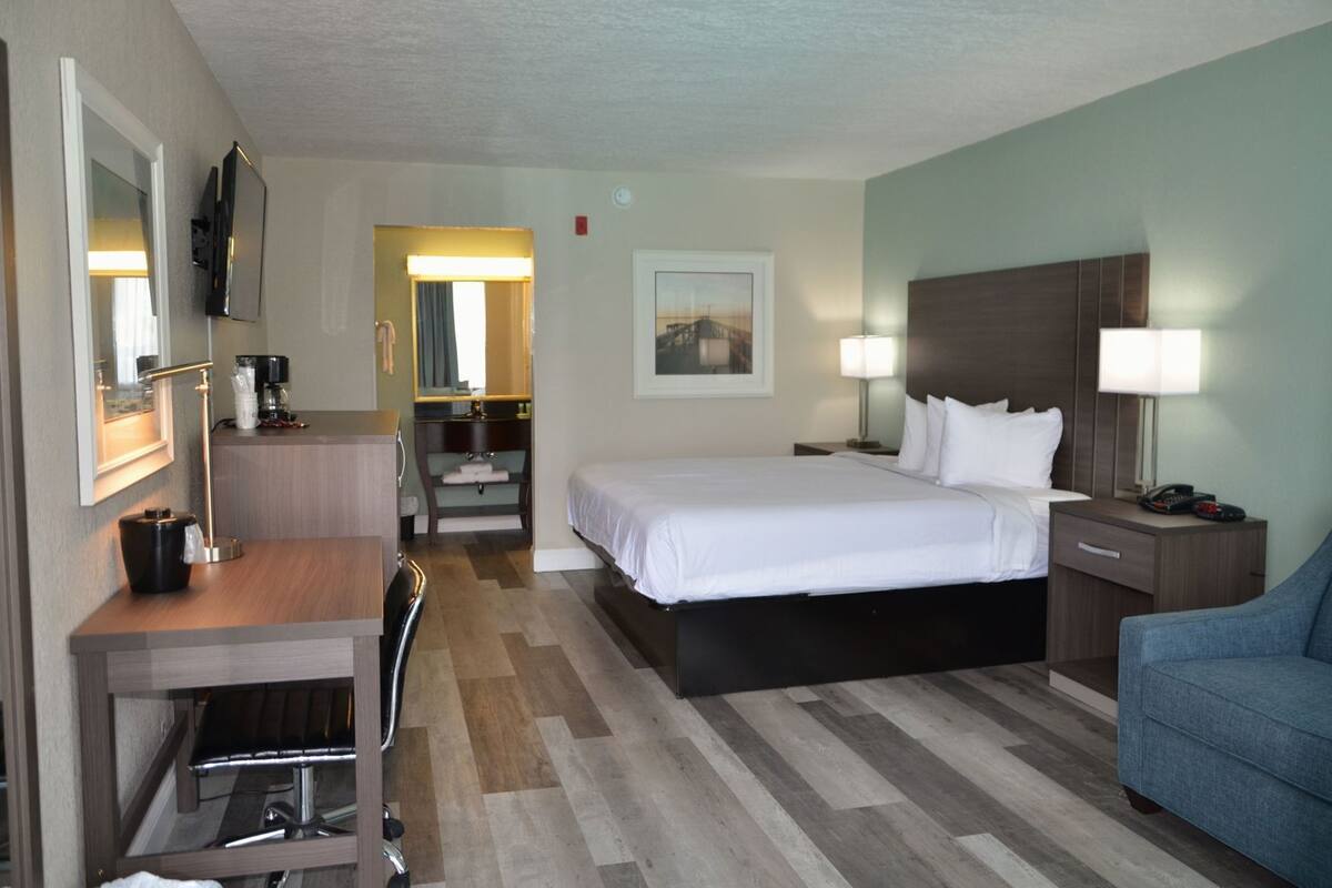 Habitación de hotel con cama, escritorio, silla, mesitas de noche, lámparas y televisión.