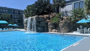 A swimming pool with a waterfall feature, surrounded by lounge chairs and umbrellas. - Opal Hotel & Suites (Altamonte Springs)