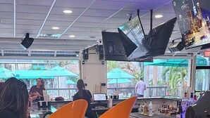 A bar area with a glass counter, orange stools, and a view of the outdoors. - Opal Hotel & Suites (Altamonte Springs)