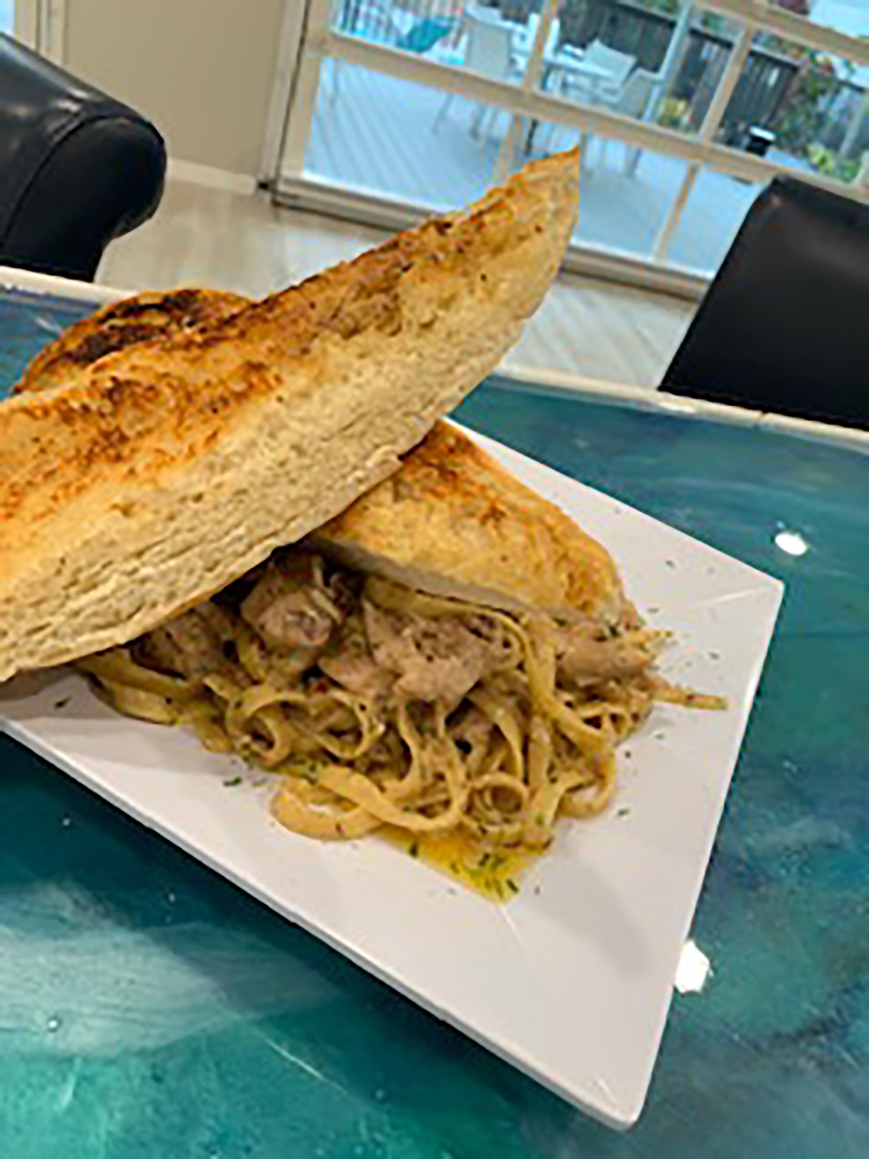 Un sandwich sur une assiette blanche, avec vue sur un bâtiment à l’extérieur.