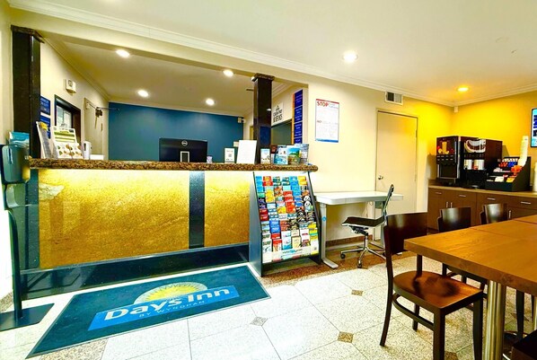 Un área de recepción con mostrador, refrigerador, cafetera, panel de menú y una puerta.