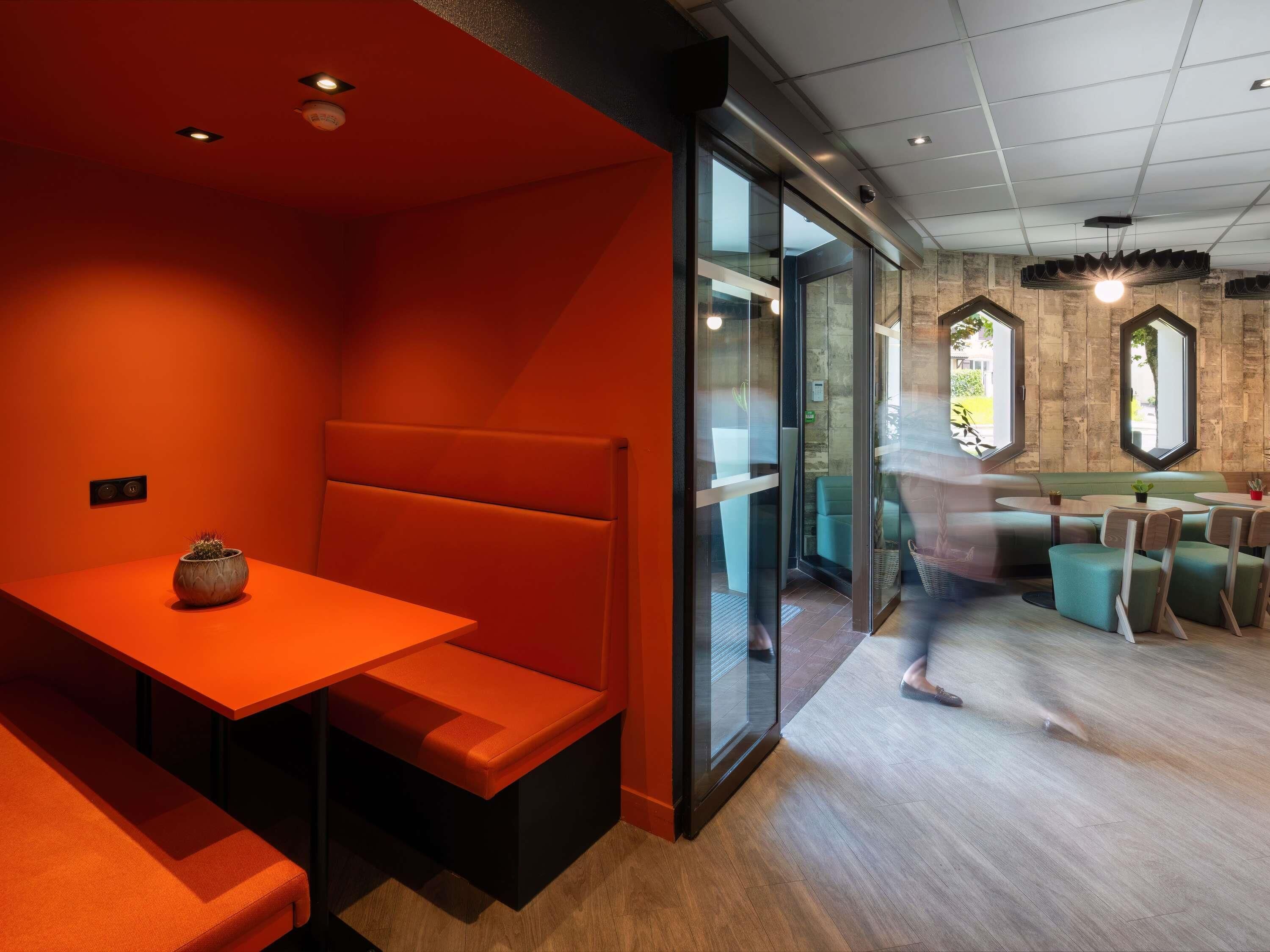 A modern interior with a seating area featuring a bench and a table, a glass partition, and a view through to another room with a bench and a table.