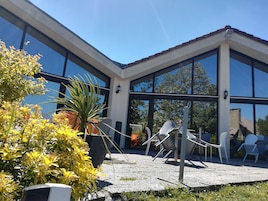 Un edificio moderno con amplios ventanales, zona de estar al aire libre con sillas y plantas en macetas.
